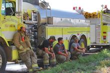 Firemen taking a break sitting next to a fire truck.
